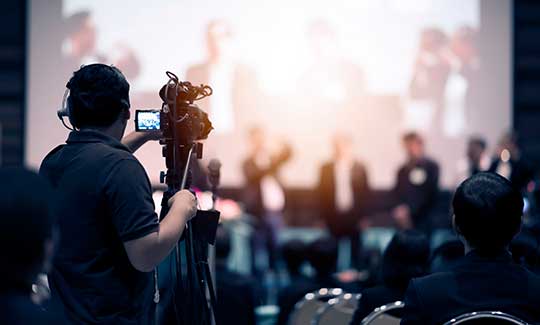 Camera operator from Audio Visual department filming at an indoor conference